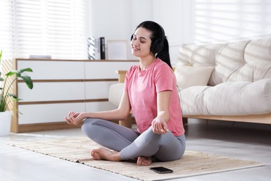 Photo of Woman with smartphone meditating on floor at home