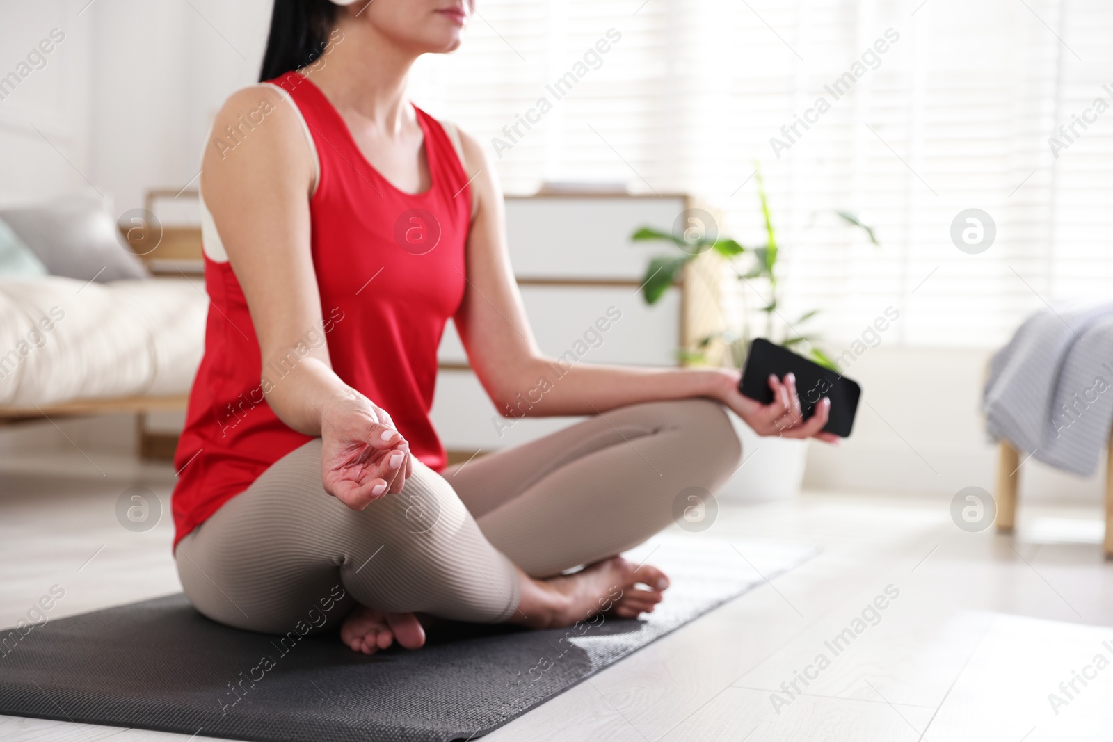 Photo of Woman with smartphone meditating on floor at home, closeup