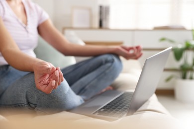 Photo of Woman with laptop meditating on sofa at home, closeup