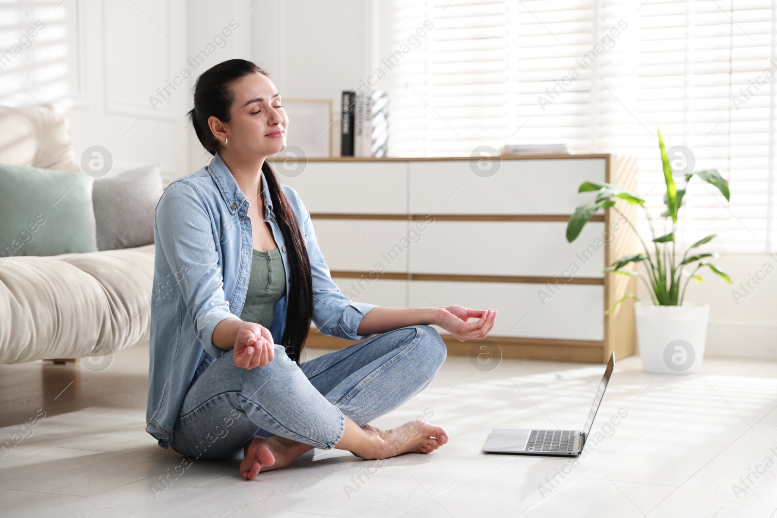 Photo of Woman with laptop meditating on floor at home. Space for text