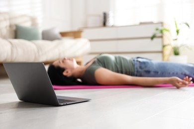 Woman with laptop meditating on floor at home, selective focus