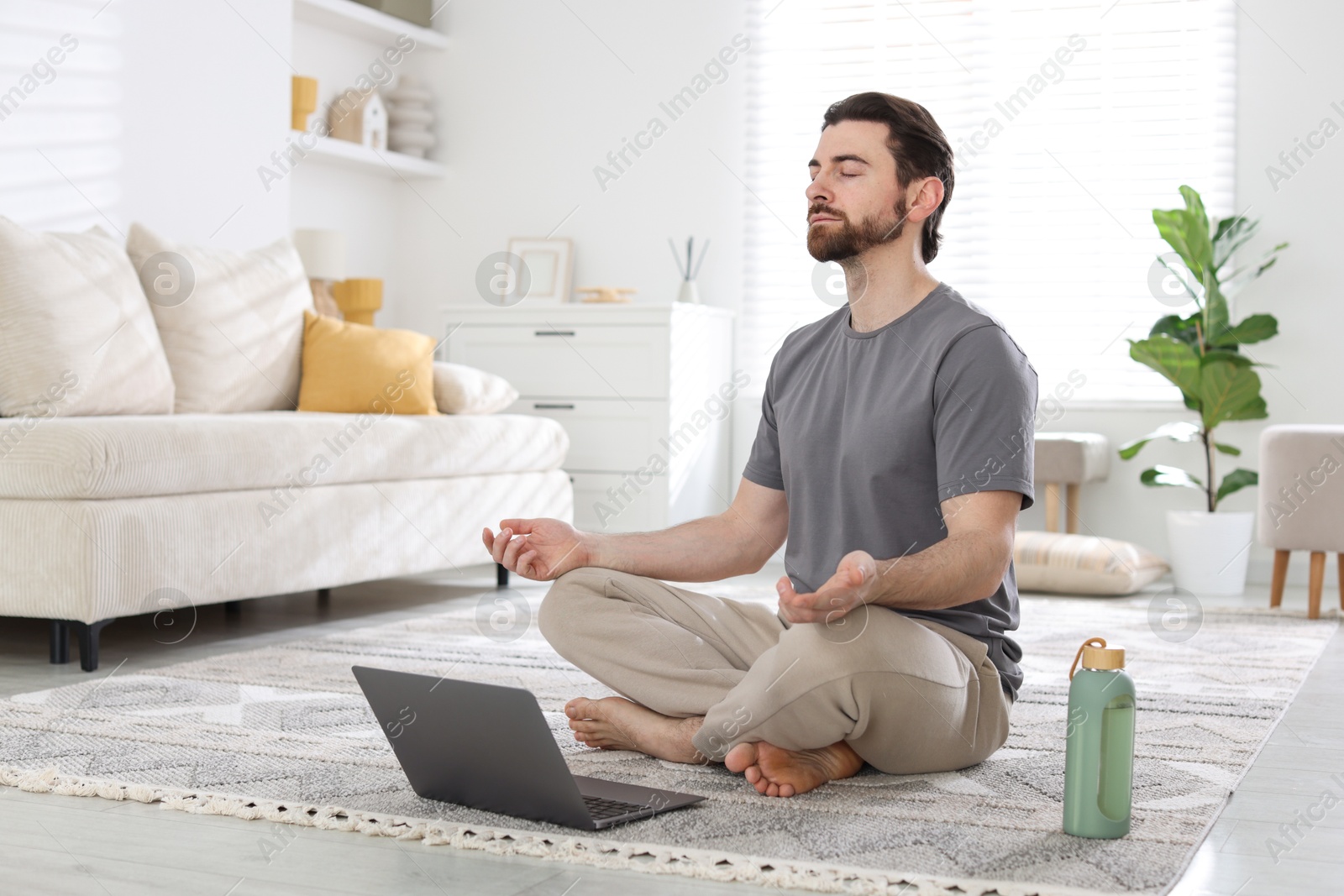 Photo of Handsome man meditating in front of laptop on floor at home