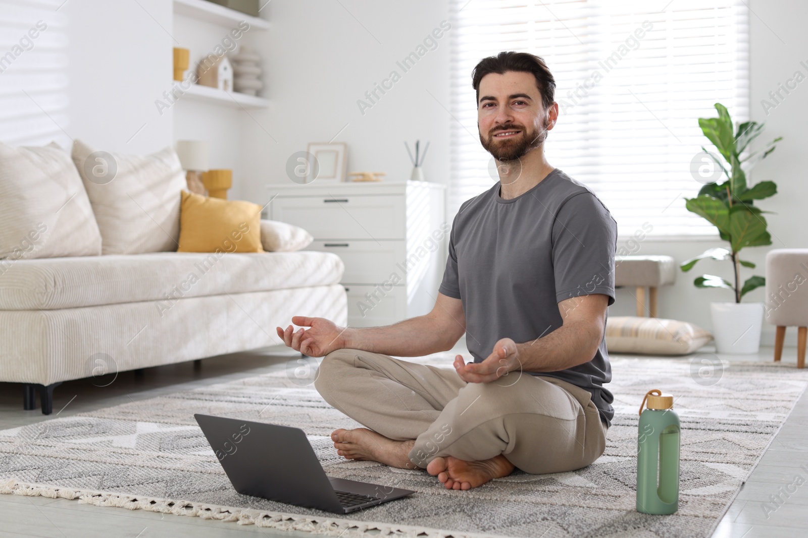 Photo of Smiling man meditating in front of laptop on floor at home