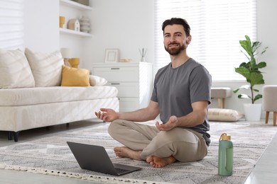 Smiling man meditating in front of laptop on floor at home