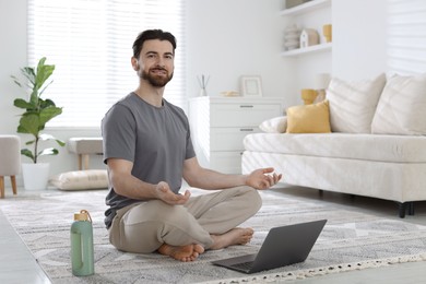 Photo of Smiling man meditating in front of laptop on floor at home