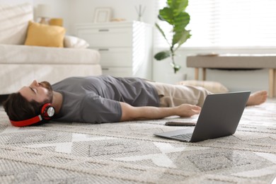 Photo of Man in headphones meditating near laptop on floor at home