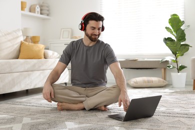 Photo of Smiling man in headphones meditating near laptop on floor at home