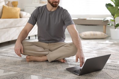 Photo of Meditation. Man watching video tutorial by laptop on floor at home, closeup