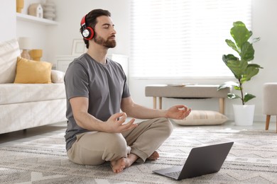 Photo of Man in headphones meditating near laptop on floor at home