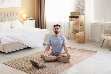 Photo of Man in headphones meditating near laptop on floor at home