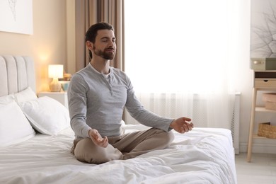 Photo of Handsome man meditating on bed at home