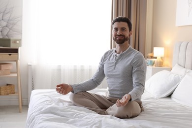 Photo of Smiling man meditating on bed at home