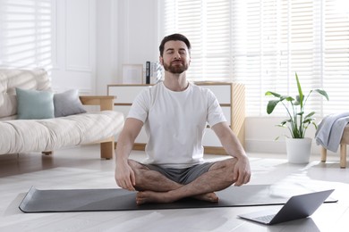 Photo of Man meditating near laptop on floor at home