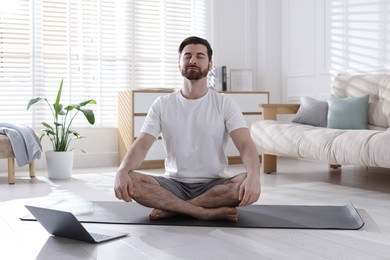 Photo of Man meditating near laptop on floor at home