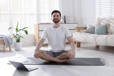 Photo of Smiling man meditating near laptop on floor at home