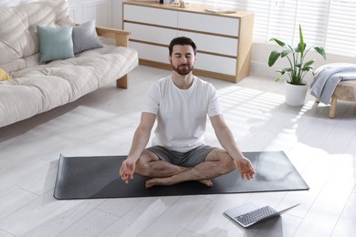 Photo of Man meditating near laptop on floor at home