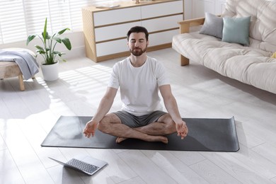 Photo of Man meditating near laptop on floor at home