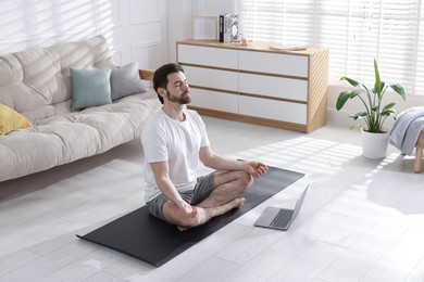 Photo of Man meditating near laptop on floor at home