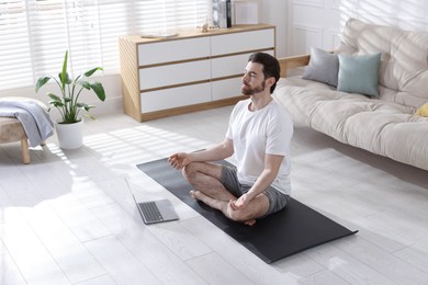 Photo of Man meditating near laptop on floor at home