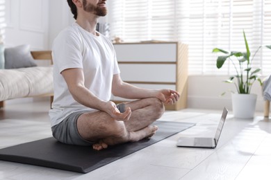 Photo of Man meditating near laptop on floor at home, closeup