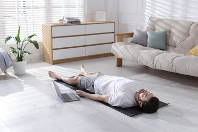 Photo of Man meditating near laptop on floor at home