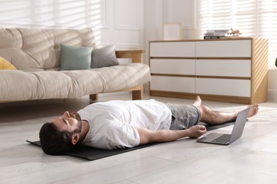 Photo of Man meditating near laptop on floor at home