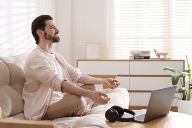 Photo of Smiling man meditating near laptop on sofa at home