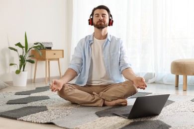 Photo of Man in headphones meditating near laptop on floor at home