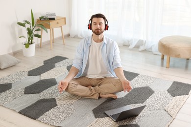 Photo of Man in headphones meditating near laptop on floor at home