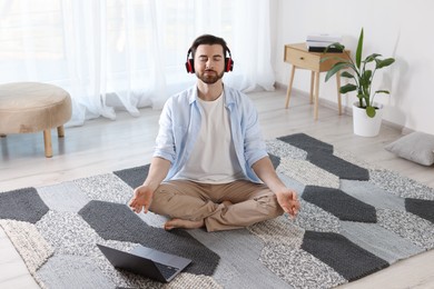 Photo of Man in headphones meditating near laptop on floor at home