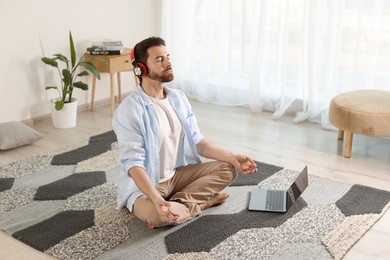 Photo of Man in headphones meditating near laptop on floor at home