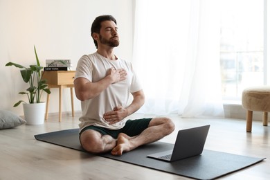 Photo of Man meditating near laptop on floor at home