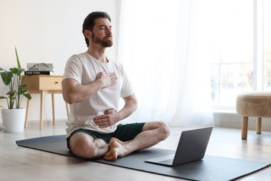 Photo of Man meditating near laptop on floor at home