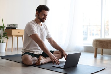 Photo of Man meditating near laptop on floor at home