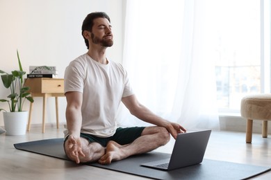 Photo of Man meditating near laptop on floor at home