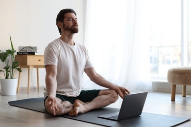 Photo of Man meditating near laptop on floor at home