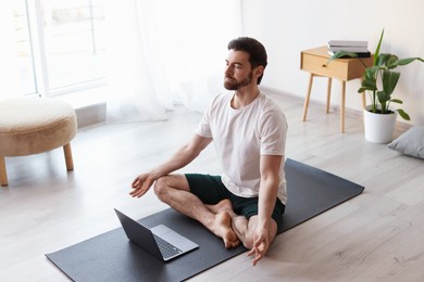 Photo of Man meditating in front of laptop on floor at home