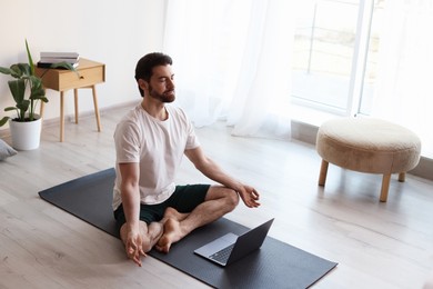 Photo of Man meditating in front of laptop on floor at home