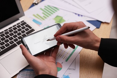 Photo of Electronic signature. Man using stylus and smartphone at wooden table, closeup