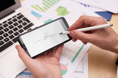 Photo of Electronic signature. Man using stylus and smartphone at wooden table, closeup