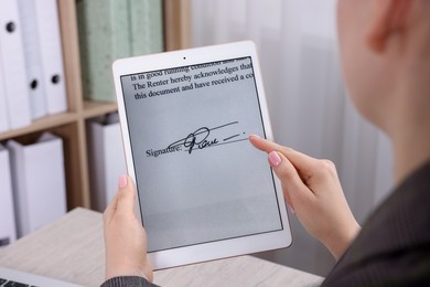 Photo of Electronic signature. Woman using tablet at wooden table indoors, closeup