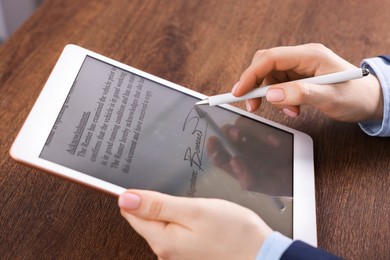 Photo of Electronic signature. Woman using stylus and tablet at wooden table, closeup