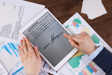 Photo of Electronic signature. Woman using tablet at wooden table, top view