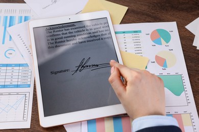 Photo of Electronic signature. Woman using tablet at wooden table, closeup