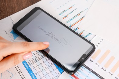 Photo of Electronic signature. Woman using smartphone at table, closeup