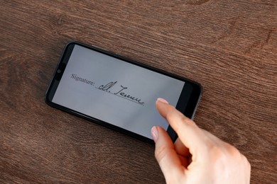 Photo of Electronic signature. Woman using smartphone at wooden table, closeup