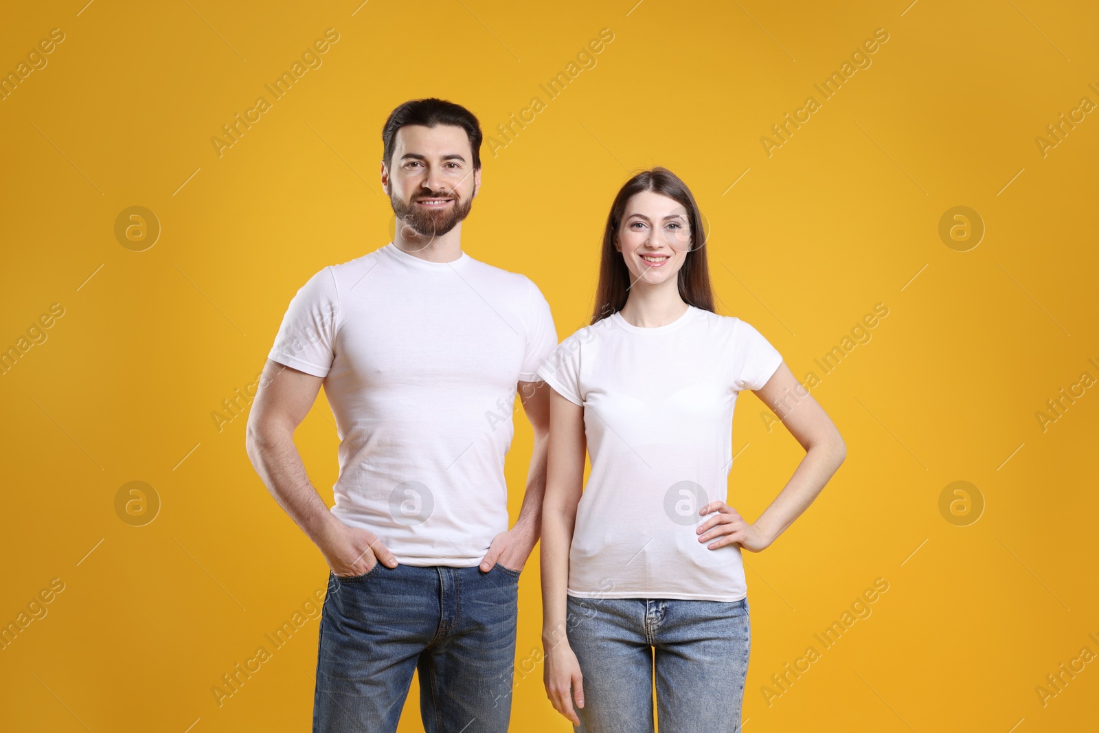 Photo of Woman and man wearing blank white t-shirts on orange background. Mockup for design