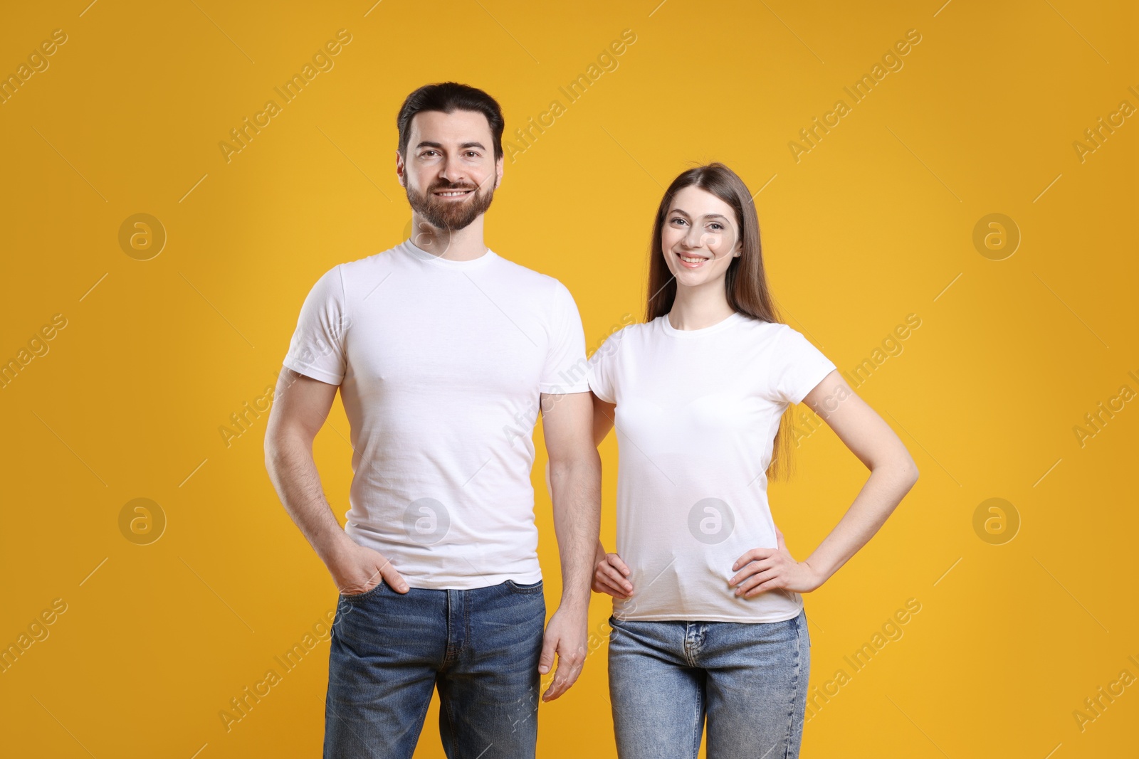 Photo of Woman and man wearing blank white t-shirts on orange background. Mockup for design