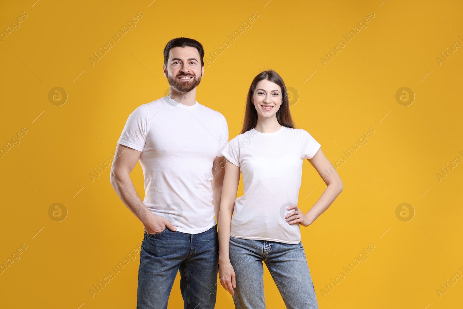 Photo of Woman and man wearing blank white t-shirts on orange background. Mockup for design