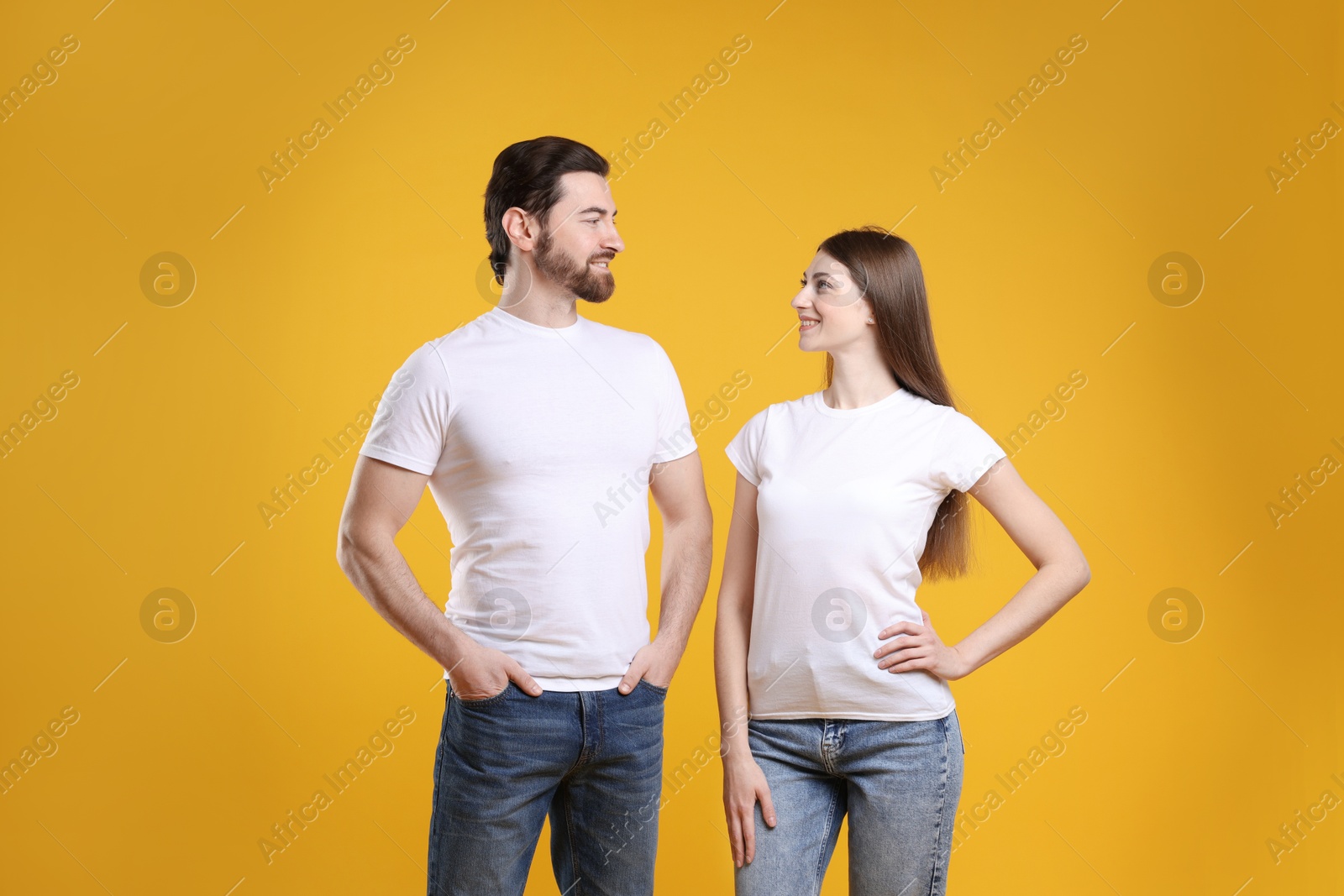 Photo of Woman and man wearing blank white t-shirts on orange background. Mockup for design